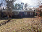 A single-story brick house with a front porch under a clear sky, located at 12698 NC 39 Highway, Henderson NC, surrounded by a lawn with scattered leaves and a bare tree in the