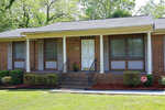 A single-story brick house located at 110 White Oak, Henderson NC, with a covered porch, white front door, and two visible windows with closed blinds. There are steps leading up to the porch