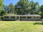 A single-story suburban house at 787 Hedrick Drive, Henderson NC, with beige siding, black shutters, a gray shingled roof, and a well-manicured lawn with a