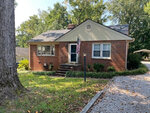 A single-story brick house with white trim, a front porch with steps, an American flag on a pole, and a large tree in the front yard at 126 Watson Drive, Henderson NC.