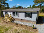 A single-story house in Henderson, NC, at 300 Madison Grove Lane, features gray siding and a brick foundation, including a small front porch with wooden stairs and landscaping with stepping stones.
