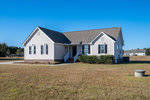 A single-story tan house with white trim and a gabled roof, located at 68 Farmington Lane, Henderson NC, features a porch with two visible windows and a front door, set on a