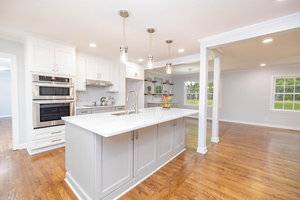 A spacious, modern kitchen with white cabinetry, marble countertops, stainless steel appliances, and hardwood flooring, featuring a central island and pendant lighting.