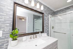 A modern bathroom featuring a large framed mirror above a white vanity, complemented by gray subway tile walls and a glass-enclosed shower area. a potted plant adds a touch of greenery to the space.