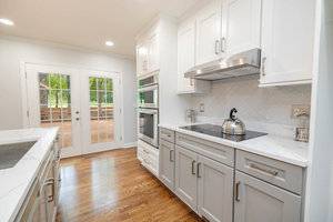 A modern kitchen featuring white cabinetry, stainless steel appliances, and hardwood floors, with abundant natural light coming from windows and a glass door leading to an outdoor deck.