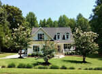 A two-story house with white siding and a gray roof is centered in a well-manicured lawn with blooming trees on either side and a clear blue sky above, located at 254 Beav