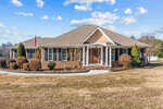 A single-story suburban home at 22 Greta Lane, Henderson NC, with a brown shingle roof, brick facade, and a landscaped yard with a paved pathway leading to an arched front