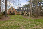A two-story brick house with white trim and a wooden front door, located at 3407 Cameron Drive in Henderson, NC, surrounded by a lawn and trees under a partly cloudy sky.