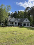 A single-story house located at 535 Franklin Lane in Henderson, NC, with a gray exterior, white trim, and an attached two-car garage, set against a backdrop of tall green trees on a
