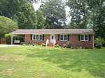 A single-story brick house located at 1517 Oakdale Circle, Henderson NC, with a white door and a carport, surrounded by a green lawn and shrubs.