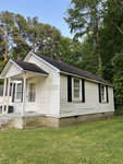 A small, white single-story house with a gabled roof and black shutters on the windows, located in a wooded area at 110 Cleveland Avenue, Henderson NC.