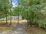 A single-story house with a red and white exterior is situated amongst trees at 700 Fred Royster Road, Henderson NC, featuring a gravel pathway leading up to the property.