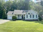 A single-story house at 85 Waterfall Road, Henderson NC, with white siding and a shingled roof, featuring a front porch with railings, a single garage door, and a well
