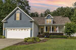 A single-story blue house with white trim and a two-car garage, located at 48 Waterfall Road, Henderson NC, features a well-manicured lawn and a small porch, under a sunset