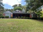 Single-story brick house with a gabled roof and dormer windows at 507 Granite Street, Henderson NC, flanked by two bay windows, set against a backdrop of trees and a clear sky,