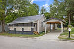 A single-story house at 920 David Street, Henderson NC, with beige siding and a dark trim, featuring a carport on the right and surrounded by trees, with a front yard mailbox by the