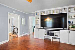 A spacious living room featuring hardwood floors, white cabinetry with a collection of trophies on display, a large flat-screen tv, and an exercise bike in the corner.