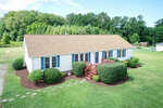 A single-story white house with a gable roof at 575 Stewart Farm Road, Henderson NC, surrounded by manicured bushes and a green lawn, featuring a small wooden deck with stairs at the front