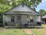A weathered single-story house at 506 Hickory Street, Henderson NC, with a front porch, featuring peeling paint and a yellow notice attached to the front, set against a backdrop of over