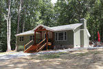 A new single-story house with green siding and a small front porch located at 1942 Kelly Road, Henderson NC, in a clearing of a wooded area.