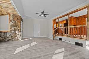 Empty room interior with gray flooring, white and stone walls, and wooden accents, featuring a ceiling fan and a railing separating different levels.