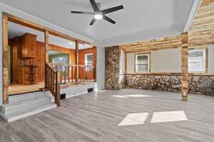 An empty room with wooden and stone wall accents, featuring a ceiling fan, hardwood floors, and a wooden railing separating an elevated section.