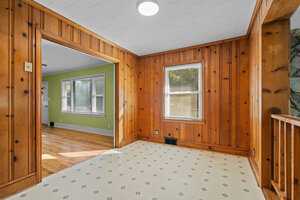 An empty room featuring hardwood floors, wood-paneled walls, a green accent wall, and two visible windows, suggesting a home interior.