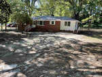 A single-story brick and white house at 118 Wester Avenue, Henderson NC, with a set of metal stairs leading to a side door, surrounded by trees casting shadows on the ground in front of