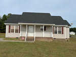A single-story house with a symmetrical facade, located at 126 Wheat Lane, Henderson NC, featuring a central front door with sidelights, flanked by double windows, a front porch with white