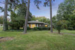 A single-story house at 346 Willowood Drive, Henderson NC, is partially obscured by trees with illuminated windows at dusk.