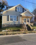 Two-story yellow house at 432 N Chestnut Street, Henderson NC, with a covered front porch and a set of stairs leading up to the entrance, seen during the day with clear skies.