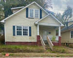 A two-story yellow house with white trim and a front porch in need of maintenance, located at 436 N Chestnut Street, Henderson NC, displays signs of wear and weathering on the exterior.