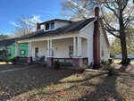 An old, weathered single-story house with a porch and missing roof sections at 312 E Andrews Avenue, Henderson NC, stands neglected, surrounded by fallen leaves and bare trees under a clear blue sky