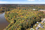 Aerial view of a landscape in Henderson NC, showing a mix of autumn-colored trees with a body of water to the left and residential buildings to the right.