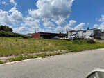 Industrial buildings behind a vacant lot with overgrown grass under a cloudy blue sky at 00 Montgomery Street, Henderson NC.
