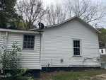A white single-story house at 501 Hillside Avenue, Henderson NC, with vinyl siding, a single window, and various cables running along its exterior. A satellite dish is installed on the side,