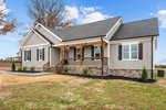 Newly constructed single-story home at 3217 Satterwhite Point Road, Henderson NC, with a gabled roof, featuring a covered front porch with wooden railings, stone veneer accents,