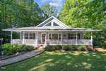 A single-story house at 136 Waters Edge Loop Rd, Henderson NC, with a covered front porch, surrounded by trees and adorned with decorative elements, set in a well-maintained lawn.