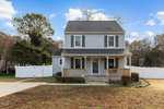 A two-story house with gray siding and a front porch, featuring a white picket fence on a clear day at 105 Quail Ridge, Henderson NC.