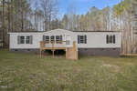 A single-story modular home with a small wooden front deck and stairs, set against a background of tall trees at 79 Redwing Lane, Henderson NC.