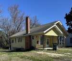 A single-story yellow house with a red brick chimney and a partially brick façade under a clear blue sky, located at 267 Chavasse Avenue in Henderson, NC.