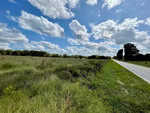 A rural road stretches beside a lush field under a partly cloudy sky, with power lines running parallel to the road and a forest in the distance at 0095 Walter Grissom Road, Henderson NC