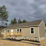 A new beige single-story house at 447 Plum Nutty Road, Henderson NC, with a small wooden porch and steps, located in a freshly landscaped area with bits of grass and several small shr