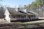 A single-story house with a gabled roof and large front porch, located at 3611 Thomas Road in Henderson NC, is surrounded by a wooded area with leafless trees under a clear blue sky