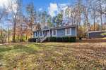 A single-story, gray house with white trim, a front porch, and steps at 205 Beavertail Road, Henderson NC, surrounded by leafy trees and a lawn scattered with fallen leaves