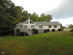 A large white house at 174 Summer Breeze Lane with a gabled roof and attached deck, surrounded by a lush green lawn and wooded area under a cloudy sky.