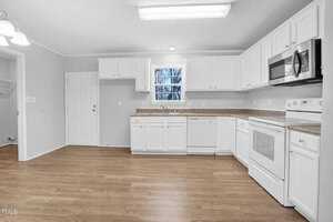 A modern kitchen with white cabinetry, stainless steel appliances, and a granite countertop. the room features wooden flooring and a view of trees through a window.