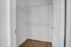 Empty walk-in closet featuring white walls and built-in wire shelving, with a hardwood floor and an open door frame.