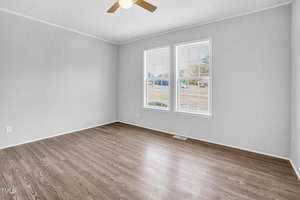 An empty room with light gray walls and laminate flooring featuring a large window with a street view and a ceiling fan.