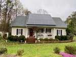 A quaint, single-story white house located at 1506 Peace Street, Henderson NC, with a large array of solar panels on the roof. The house features a front porch with a red door and